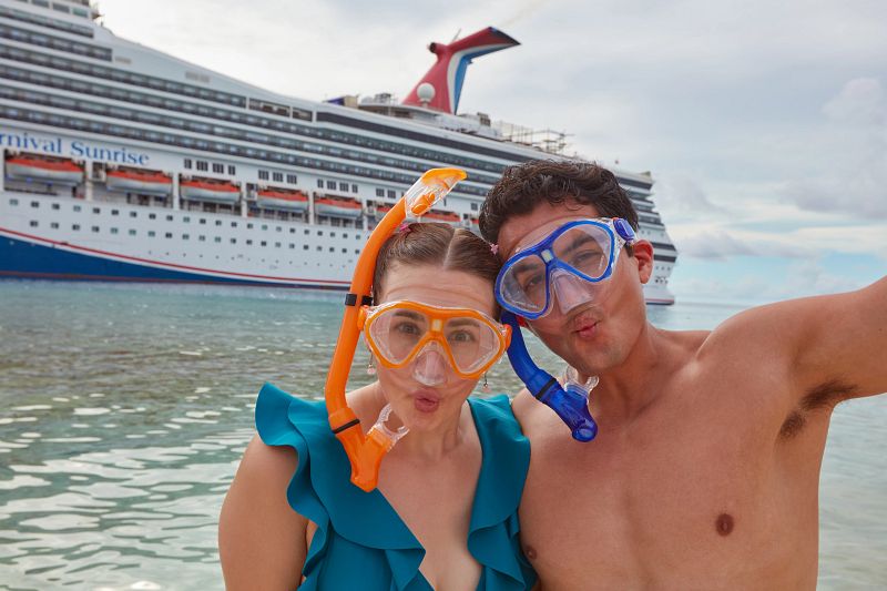 Carnival cruisers taking a quick photo with the cruise ship behind them before diving for a refreshing swim
