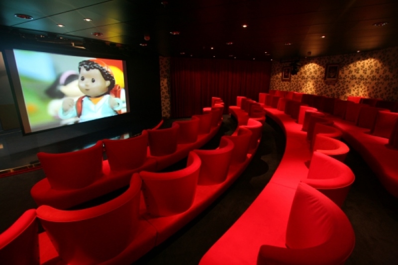 The cozy Adventure Theater on Allure of the Seas, featuring plush red seats and a large screen displaying colorful animation, providing an intimate movie experience for passengers.