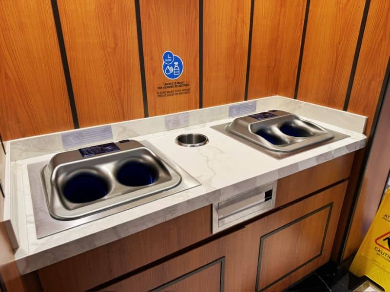 An automated hand washing station on a Costa cruise ship, featuring motion-activated soap dispensers and sinks, encourages hygiene with a convenient and contactless method, set against a backdrop of warm wood paneling.