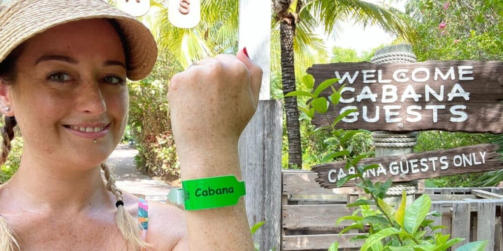 Cruise Mummy at a tropical resort, showcasing her green "Cabana" wristband, which likely grants her access to exclusive cabana areas. She is posed next to a rustic wooden sign reading "Welcome Cabana Guests," surrounded by lush greenery, indicating a serene and exclusive environment. Cruise Mummy is dressed in casual resort wear with a wide-brimmed hat, ideal for a sunny day outdoors. This setting conveys a relaxed and privileged vacation experience, with access to special guest areas enhancing her enjoyment.
