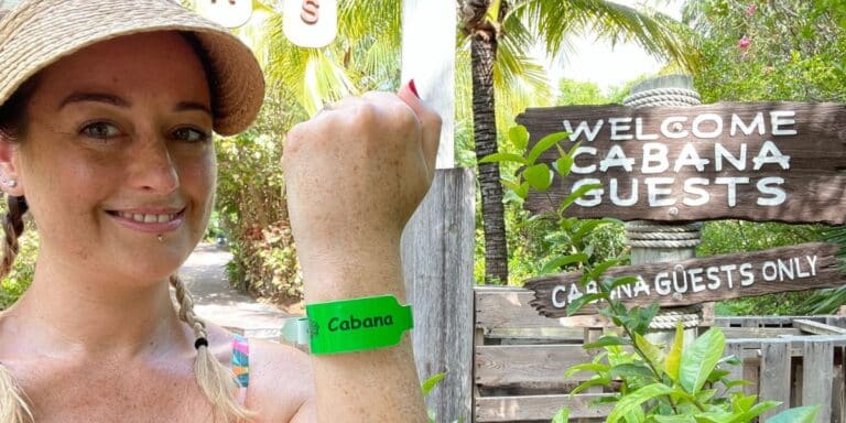 Cruise Mummy at a tropical resort, showcasing her green "Cabana" wristband, which likely grants her access to exclusive cabana areas. She is posed next to a rustic wooden sign reading "Welcome Cabana Guests," surrounded by lush greenery, indicating a serene and exclusive environment. Cruise Mummy is dressed in casual resort wear with a wide-brimmed hat, ideal for a sunny day outdoors. This setting conveys a relaxed and privileged vacation experience, with access to special guest areas enhancing her enjoyment.