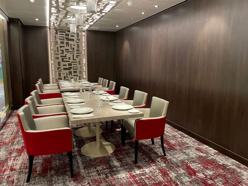 Elegant private dining room on a Carnival Cruise ship, showcasing a long, marble-topped table with cream and red chairs, set for a group meal, complemented by a patterned carpet and stylish geometric wall paneling.