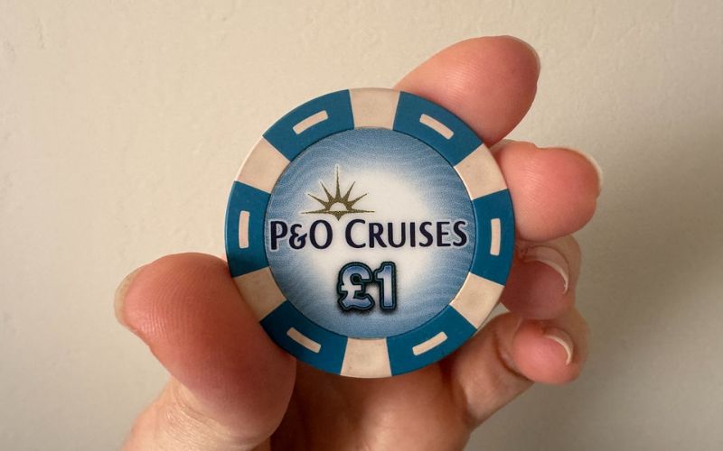 My hand holding a blue and white P&O Cruises casino chip with a £1 denomination, typically used as currency for onboard casino games or as a collectible souvenir.