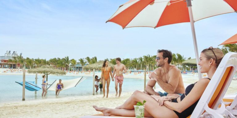 A man and woman sat next to a man at CoCo Cay on the beach.