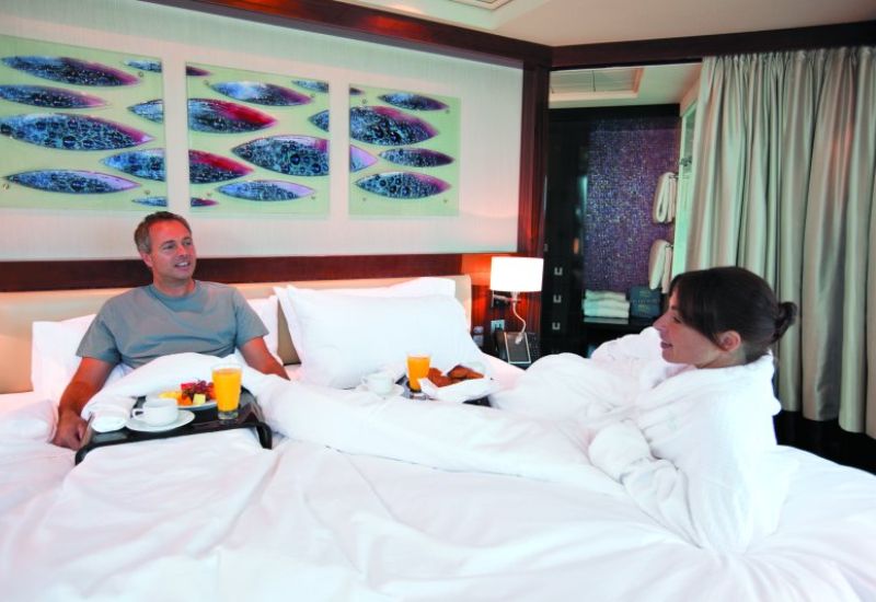 Couple on NCL stateroom talking over breakfast in bed