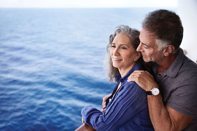 A serene image of a mature couple embracing on the deck of a Princess cruise ship, with the vast ocean stretching into the horizon behind them, capturing a moment of tranquility and togetherness at sea.