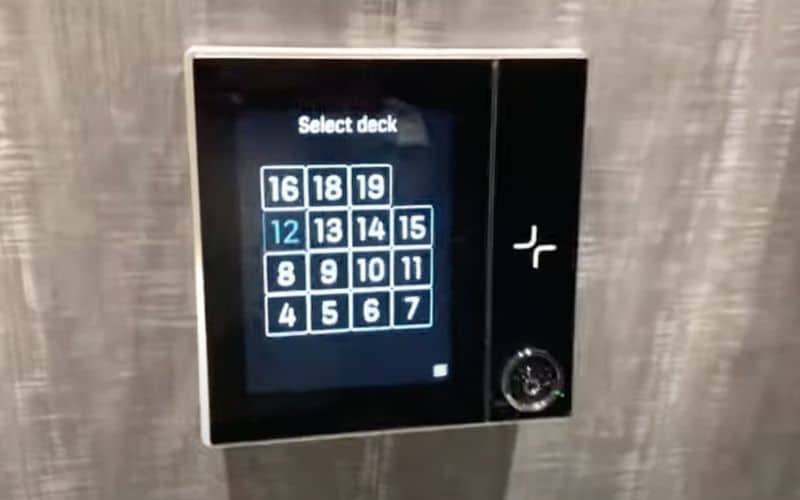 A touch screen elevator control panel on a cruise ship, displaying deck numbers for passengers to select their desired floor, modernizing the experience with its sleek digital interface against the metal elevator wall.