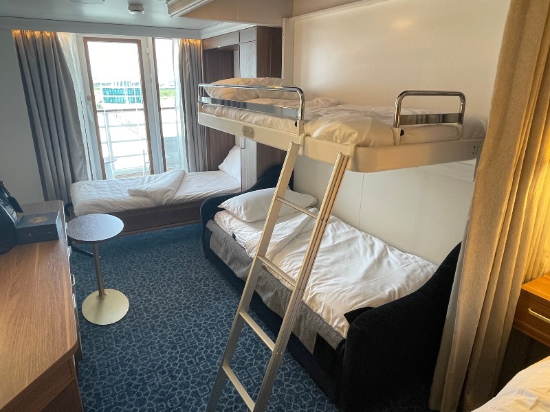 Interior of a Deluxe Family Oceanview Stateroom with Verandah on the Disney Wish, featuring a neatly made lower bed and an upper bunk bed with a ladder, by a window offering a view of the sea.