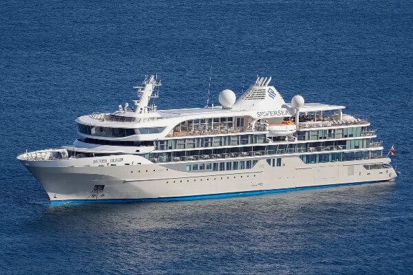 The Silver Origin, an expedition ship from Silversea Expeditions, is pictured in the middle of the blue ocean, displaying its sleek design with distinctive white and teal color scheme and the Silversea logo on the funnel.