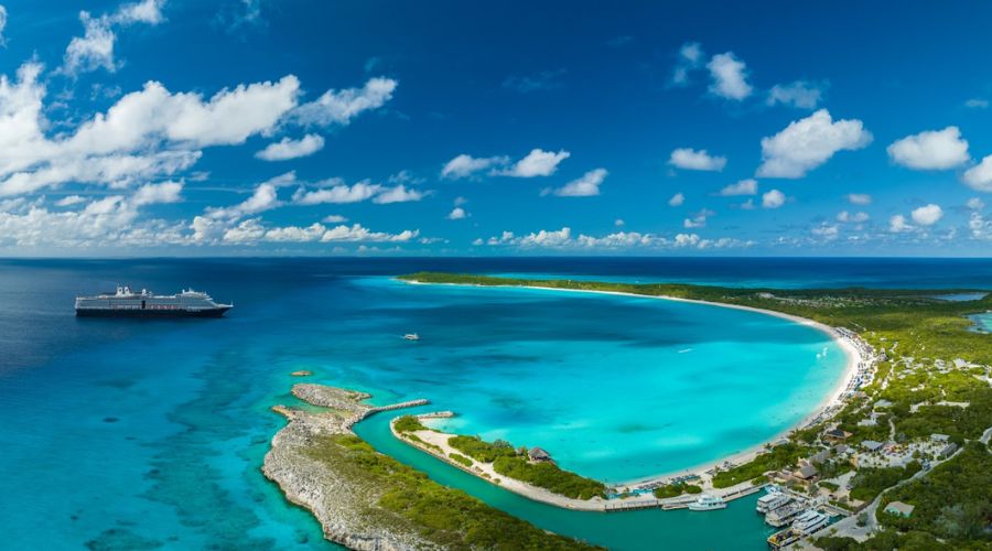 Breathtaking aerial view of a Holland America Line cruise ship floating near the expansive, crescent-shaped Half Moon Cay. The ship's grandeur is juxtaposed against the island's vibrant turquoise waters, white sandy beach filled with visitors, and lush green interior, encapsulating the essence of a luxury tropical getaway.