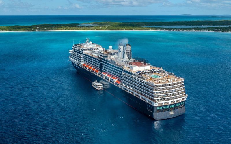 An impressive Holland America Line cruise ship anchored off a tropical coast, its multiple decks and rows of balconies gleaming under the sun. Tenders ferry passengers to the lush island, promising a day of exploration amid the stunning backdrop of clear blue waters and verdant landscapes.