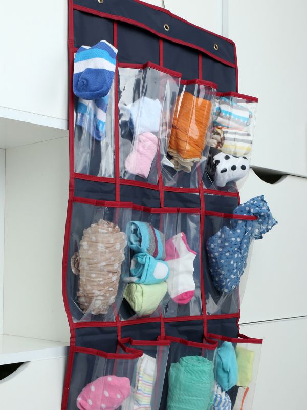 A hanging storage organizer is seen on a cruise ship, featuring multiple clear pockets filled with various items such as rolled-up socks and small clothing articles. The organizer is made of navy blue fabric with red trim and is neatly hung against a white background, maximizing space efficiency in the cabin.