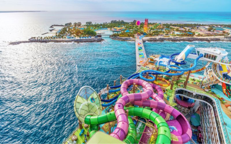 A vibrant aerial view of the Icon of the Seas cruise ship's water slide, featuring an array of colorful tubes that twist and turn above the deck against a backdrop of the expansive sea and a tropical island