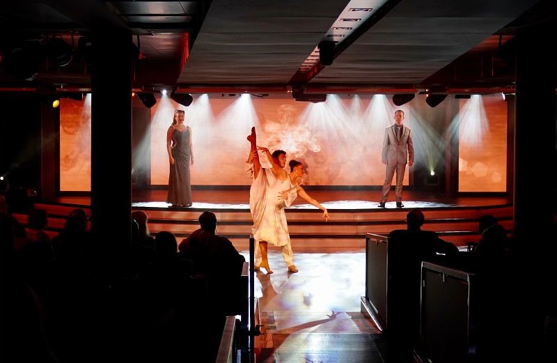 A captivating live dance performance on a Seabourn cruise ship, with performers gracefully moving on stage under dramatic lighting, while an audience watches intently, immersed in the cultural experience.