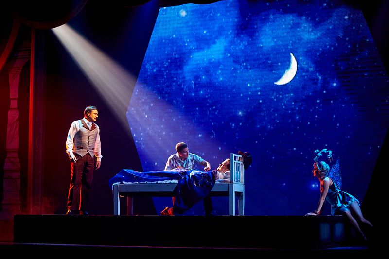 A scene from the 'Magic To Do' Production Show titled 'Prestidigitation' on a Princess Cruise ship, featuring performers in vibrant costumes on stage with dramatic lighting and a backdrop of a starry night sky and crescent moon.