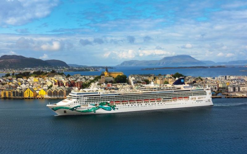 Ncl cruise ship preparing to dock beside a beautiful island with a bunch of colorful houses.