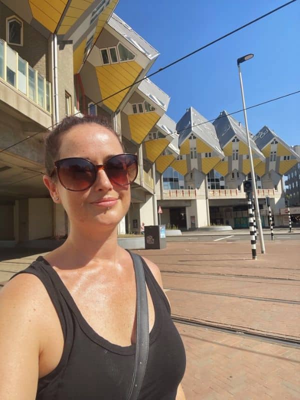 Cruise Mummy with sunglasses takes a selfie in front of the unique cube houses in Rotterdam, Netherlands, during a Princess Cruises shore excursion. The distinctive yellow and gray buildings stand out under a clear blue sky.