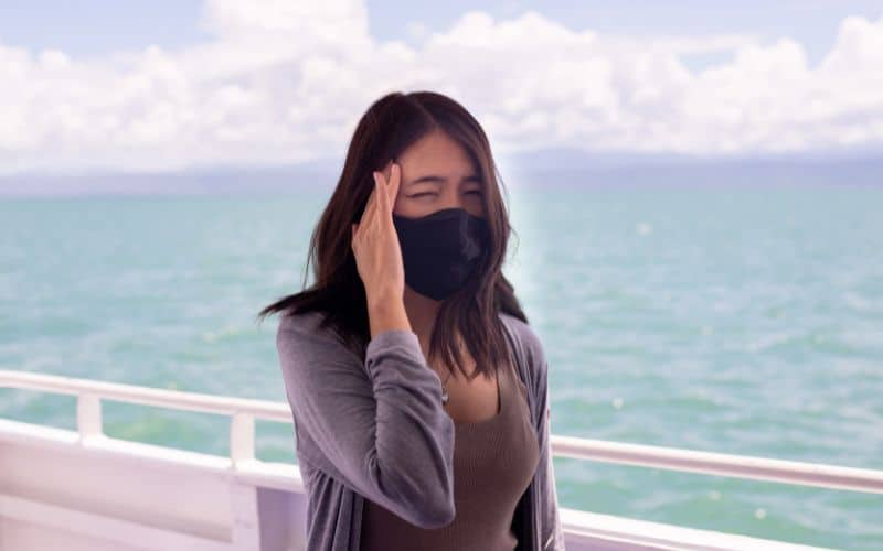 A sick lady onboard wearing a black face mask while rubbing her achy head