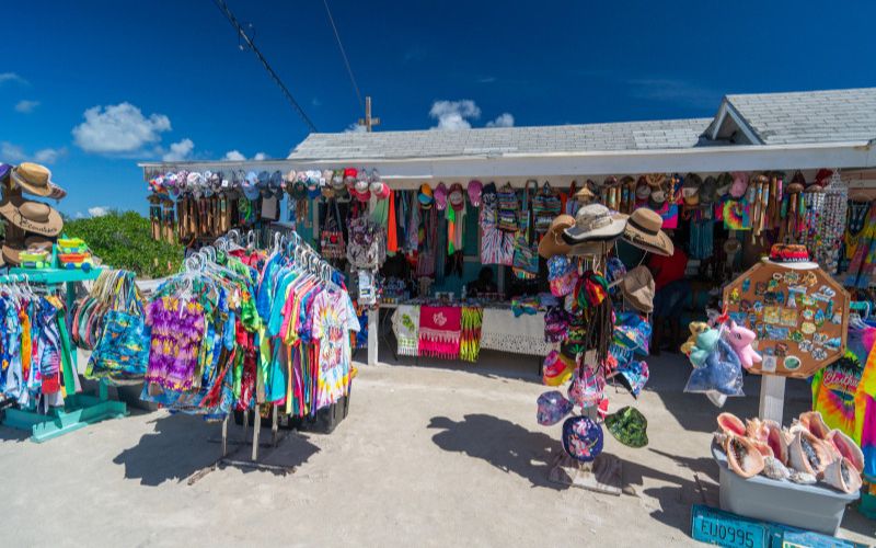 A bustling souvenir shop under a bright blue sky offers a colorful array of beachwear, hats, and local crafts. The vibrant merchandise reflects the lively spirit of a tropical vacation, inviting tourists to take a piece of paradise home with them.