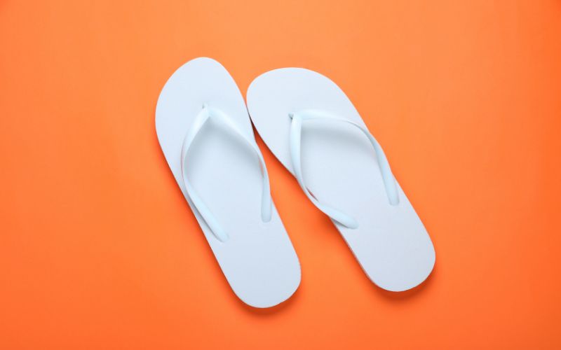 A pair of white flip-flops laid out neatly on a vibrant orange background, suggesting a summer or beach theme, often associated with cruise ship vacations or spa amenities.