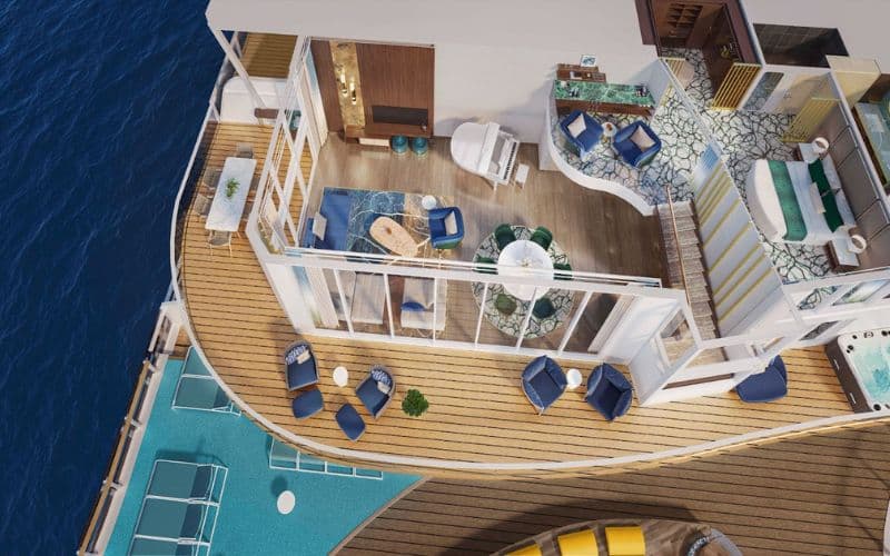 Aerial view of a luxurious suite on Royal Caribbean's 'Star of the Seas.' The suite features an expansive balcony with multiple lounging areas, both shaded and sunlit, furnished with blue and white upholstered chairs and sofas. Inside, the suite is elegantly decorated with a plush seating area, a dining space, and private sleeping quarters, all designed with a cohesive nautical theme.