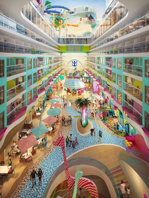 Vibrant and colorful view of the Surfside neighborhood on Royal Caribbean's 'Icon of the Seas.' This bustling area showcases a playful design with multicolored floors, bright beach umbrellas, and various recreational activities. Overlooking this lively scene are multiple levels of staterooms with pastel-colored balconies, while towering water slides curl down into the area, enhancing the festive atmosphere.
