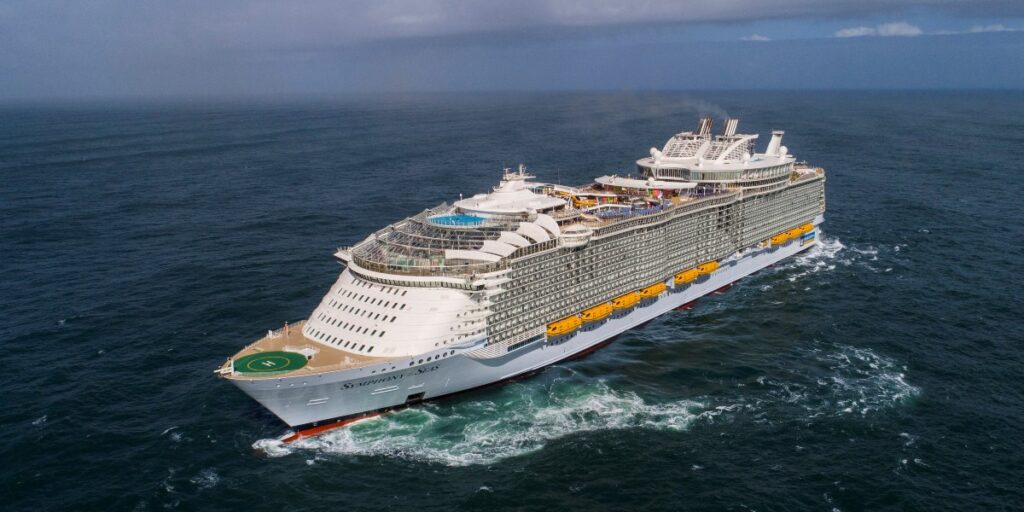 Aerial view of the 'Symphony of the Seas' cruise ship sailing on the ocean, showcasing its multiple decks and the helipad at the bow.