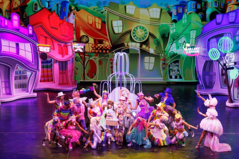 A vibrant and whimsical stage performance of 'The Wizard of Oz' on Icon of the Seas, featuring a lively cast in colorful costumes with a creatively painted backdrop depicting the whimsical city of Oz.