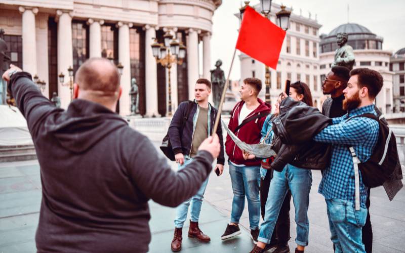 A tour guide with a red flag, showing a group of men around a city.