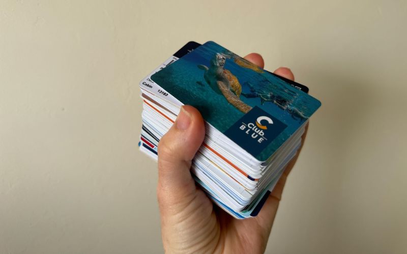 My hand holding a stacked deck of various cruise cards with the top card featuring an image of a turtle swimming in clear blue waters, representing a collection of cruise line membership or loyalty cards.
