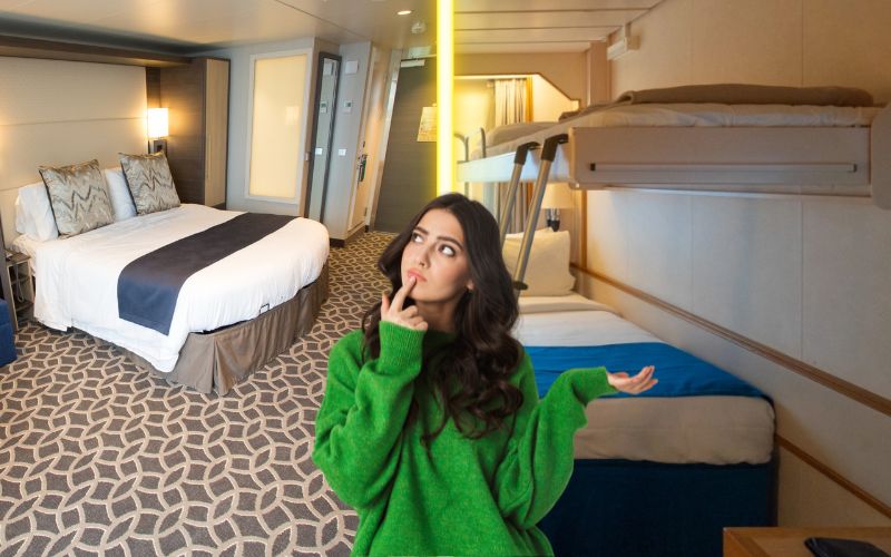 The image shows a young woman in a green sweater, posing thoughtfully in a cruise ship cabin. The cabin features a large double bed and additional bunk beds, designed to accommodate multiple passengers. The setting includes modern decor with a patterned carpet and tasteful furnishings.
