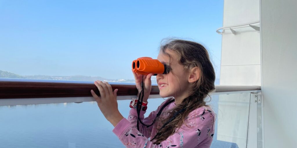 Young girl on cruise ship balcony using binoculars to look out to sea