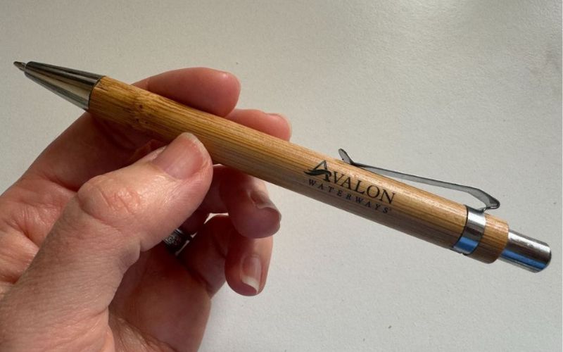 My hand holding an Avalon Waterways branded wooden pen with a sleek design and metal accents.