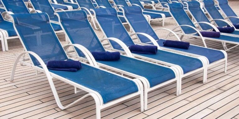A row of blue lounge chairs on a cruise ship deck, each with a neatly folded blue towel. The wooden deck adds to the clean and organized appearance, ready for guests to relax and enjoy the sun.