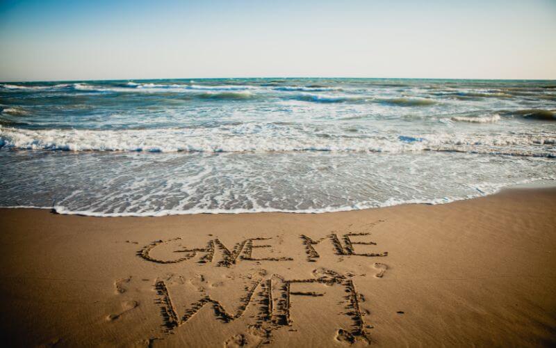 The phrase "Give me WiFi" written in the sand on a beach