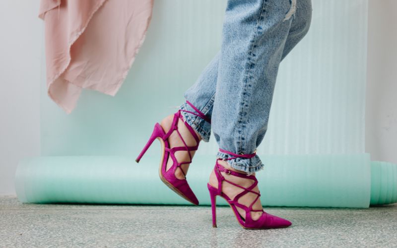  A woman in pink heels and jeans, ready for a trip, stands confidently with her luggage beside her.