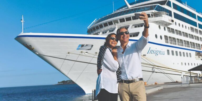 a couple taking a photo on their phone in front of a cruise ship
