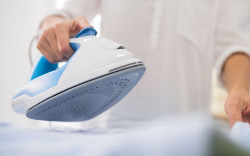 A person ironing clothes with a steam iron, focused on getting the wrinkles out of a shirt on an ironing board.