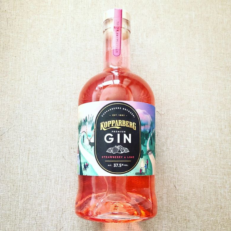 Bottle of Kopparberg Premium Gin, Strawberry & Lime flavor, with an alcohol content of 37.5%, placed on a light beige surface. The label features an illustrated scenic landscape with trees and a winding path.
