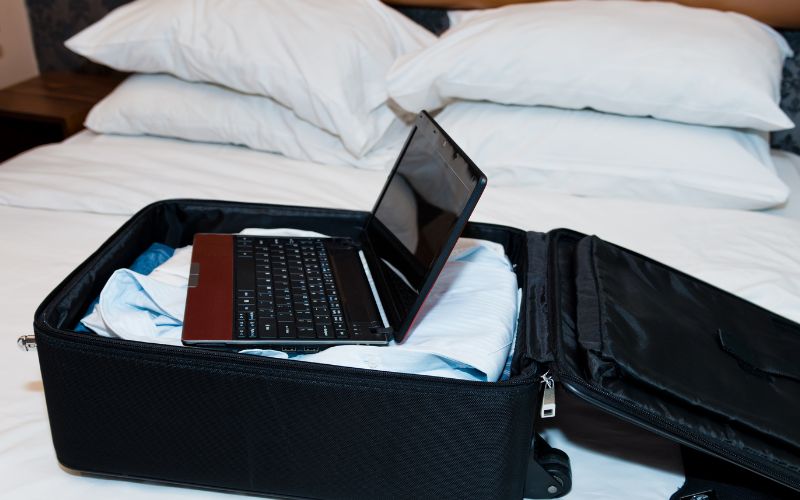 A laptop resting inside a suitcase, placed on a neatly made bed, ready for travel or a cozy work session.
