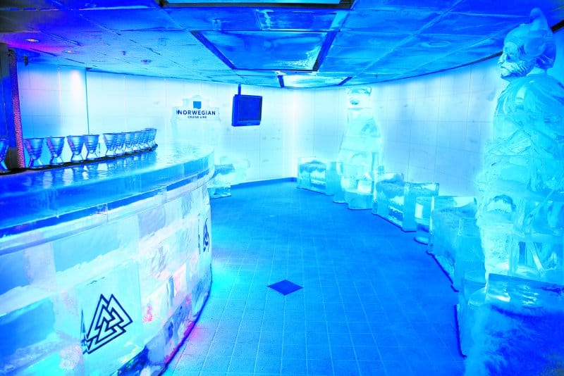 The Ice Bar on NCL Epic envelops guests in a frosty blue ambiance, with an ice-sculpted bar, seating, and figures, complete with glasses made of ice, providing a unique and chilly drinking experience aboard a Norwegian Cruise Line ship.