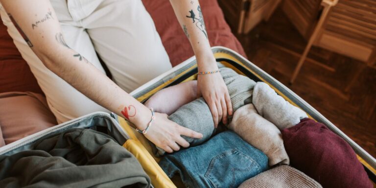 A woman with colorful tattoos is organizing her clothes into a suitcase, preparing for a trip.