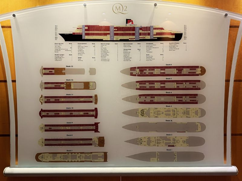 A paper deck plan of the Cunard Queen Mary cruise ship, showing labeled diagrams of each deck from Deck 1 to Deck 13. The plan includes a side view of the ship with corresponding deck sections and details on various facilities and amenities.