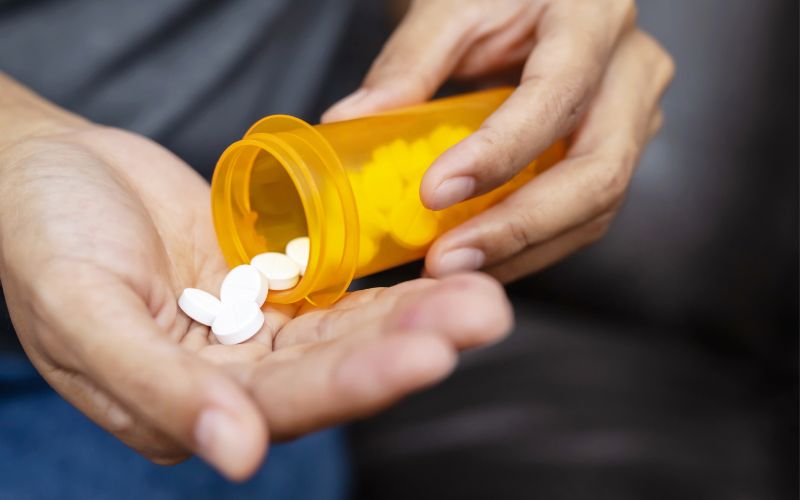 Close-up of hands pouring white pills from an orange prescription bottle, symbolizing medication management or healthcare.